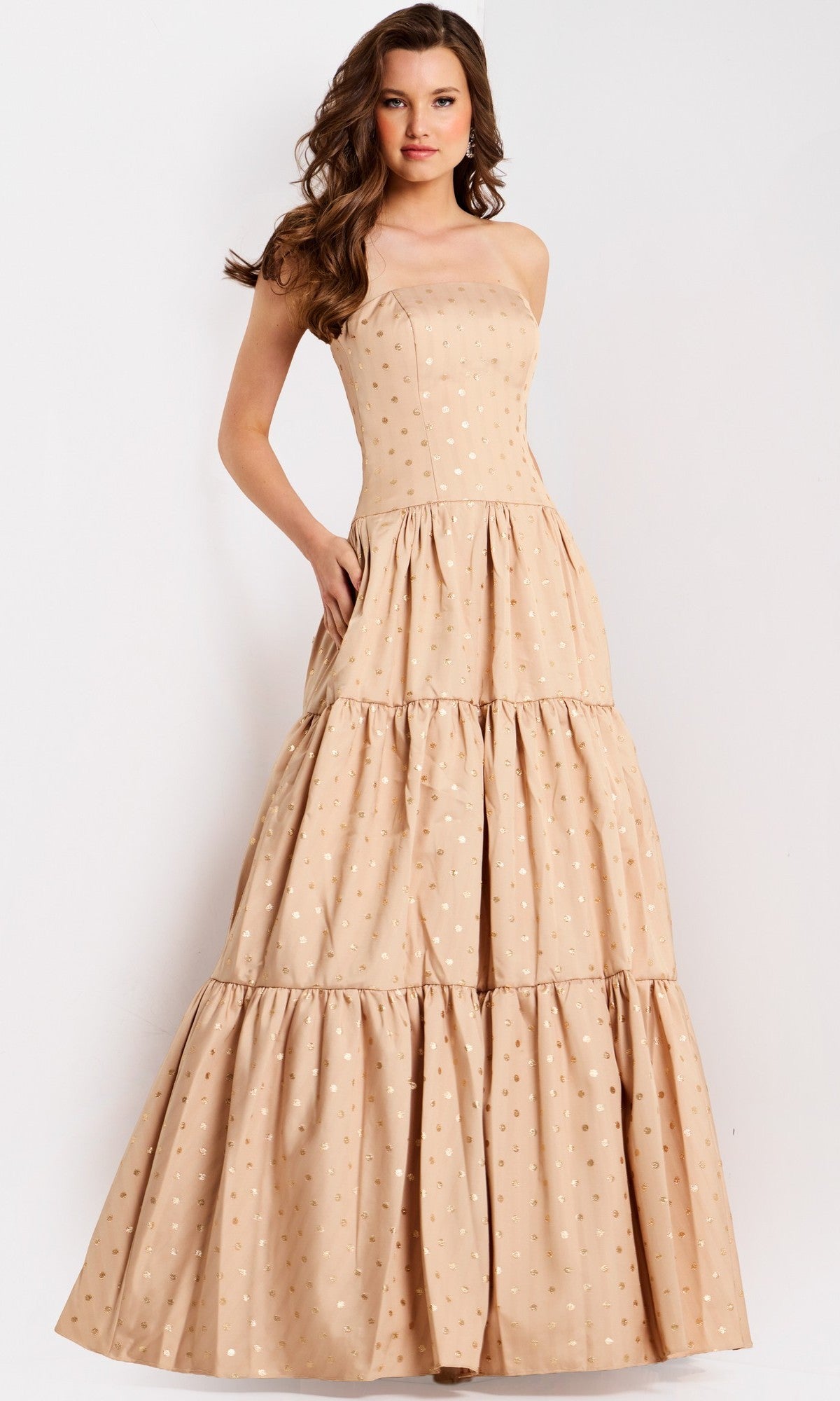 A woman wearing the Jovani 49341 long prom dress, a sleeveless beige tiered gown with subtle gold polka dots, stands against a plain white background.